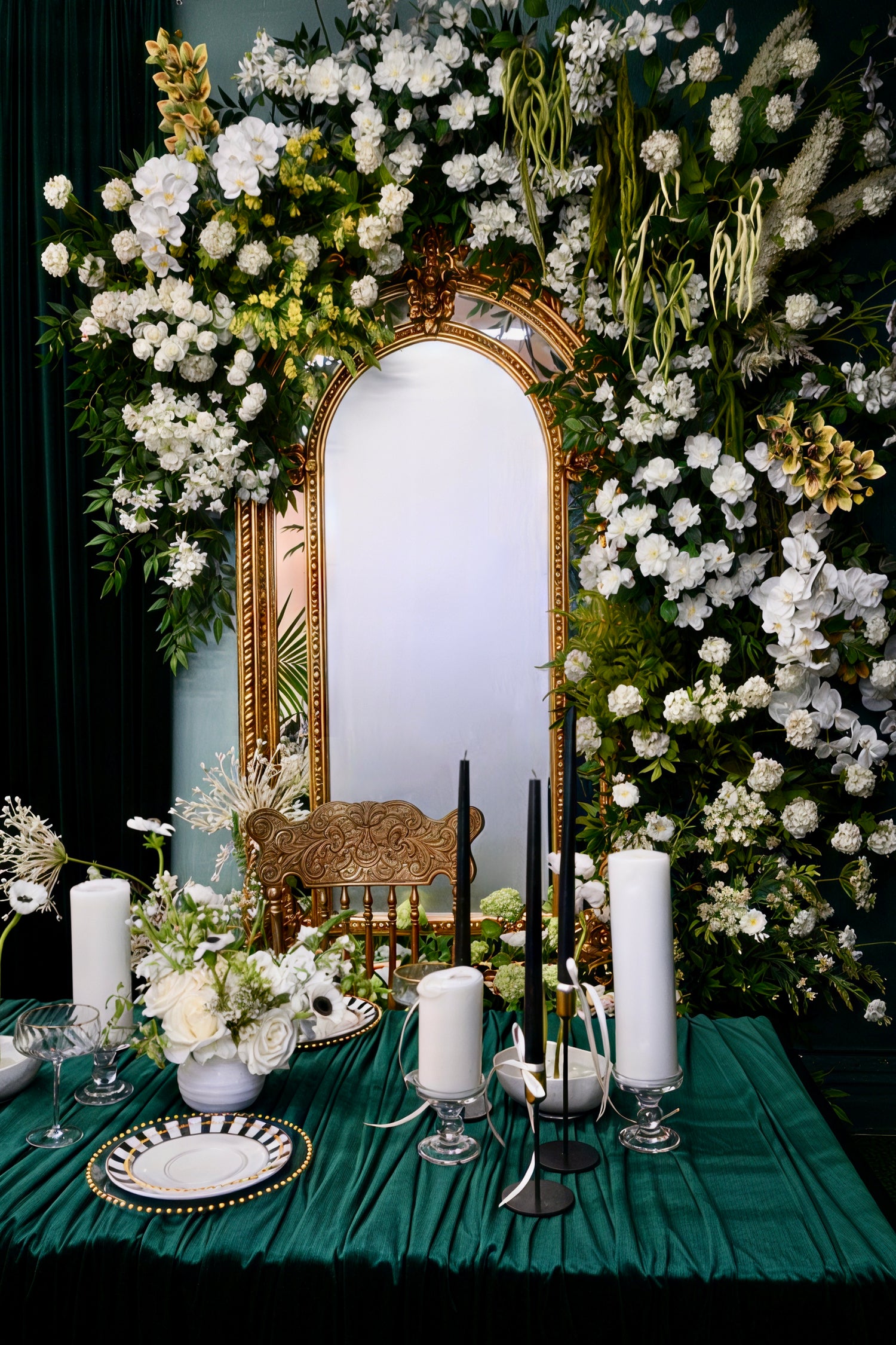 Decorative table setting with flowers, candles, and a mirror framed by floral arrangements.