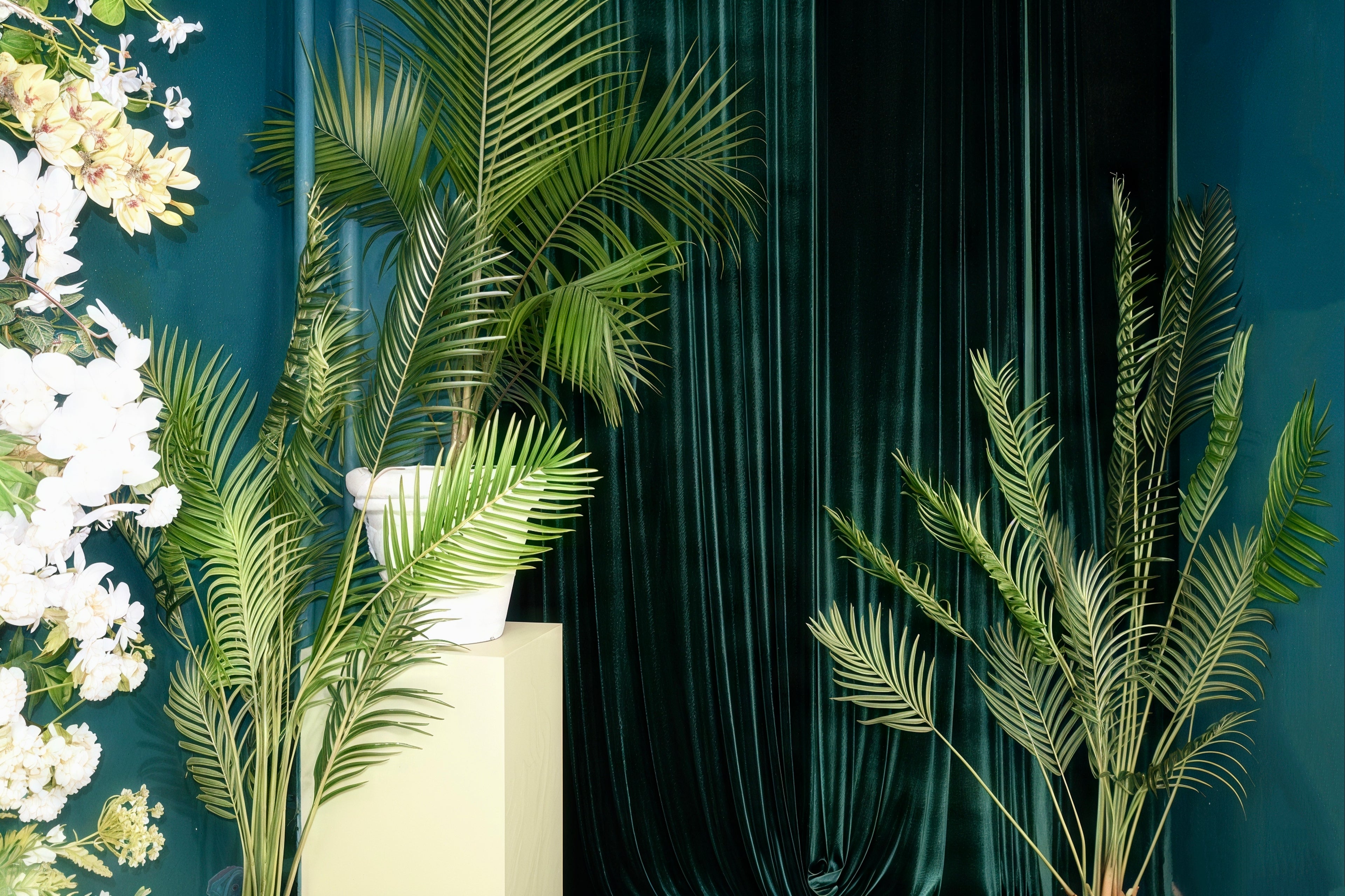 Decorative setting with green plants, white flowers, and a dark curtain.